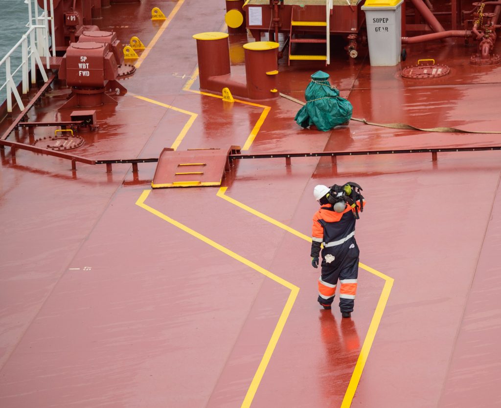 Workers on a cargo ship deck during daytime, wearing protective gear, ensuring safety compliance.